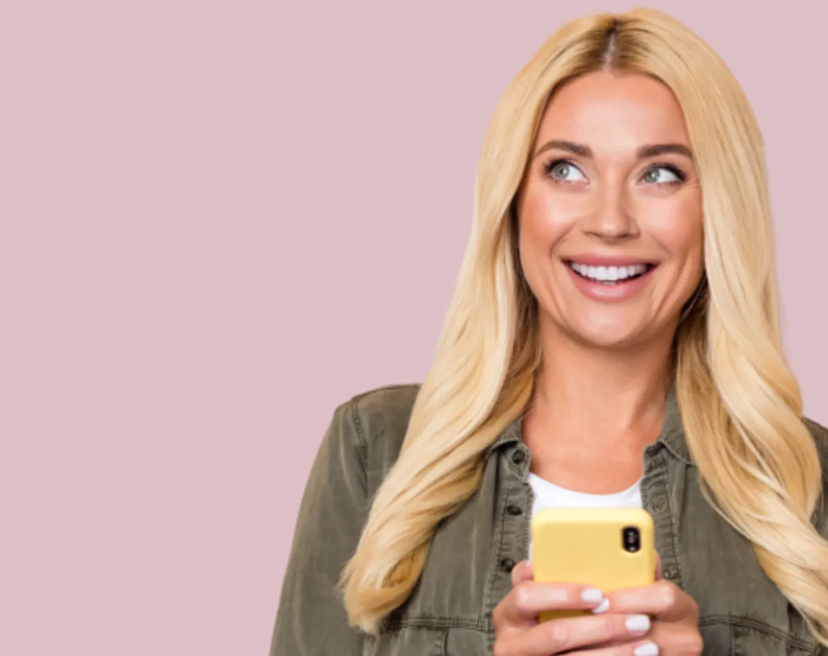 A long haired woman stares off screen with a wide smile while she holds her yellow cell phone